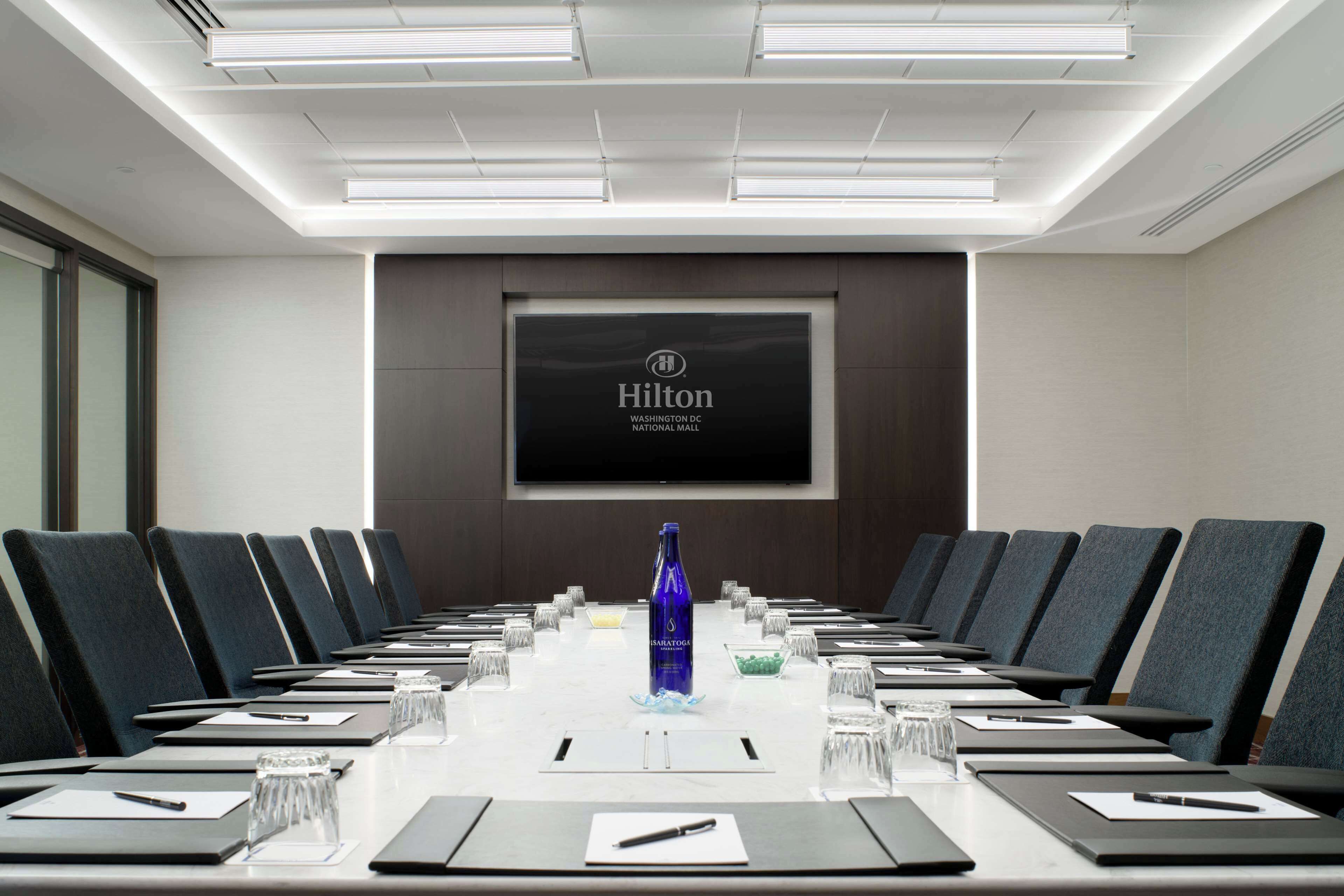 A conference room with a long table, chairs, and a projector screen displaying the Hilton logo.
