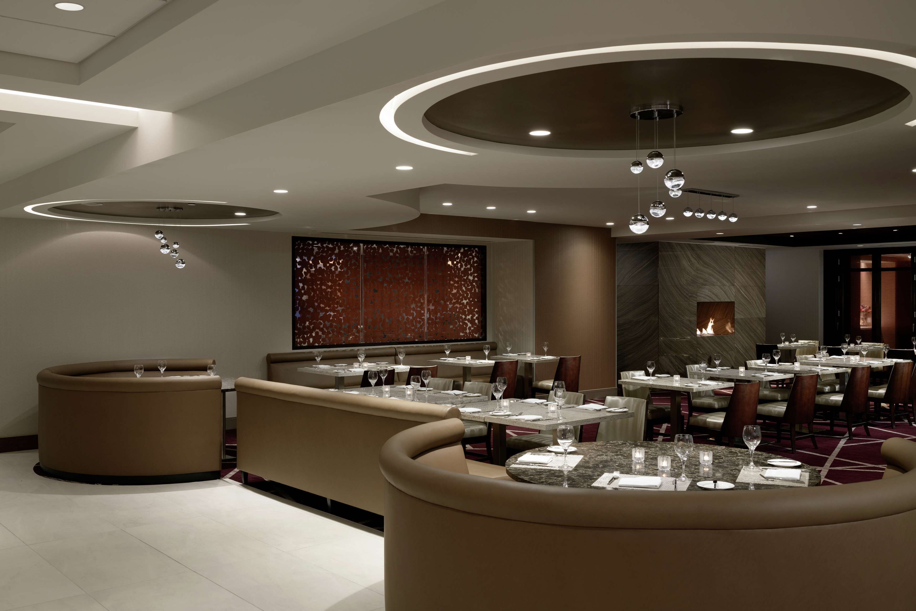 Interior moderno de restaurante com mesas redondas, cabines estofadas e uma lareira central.