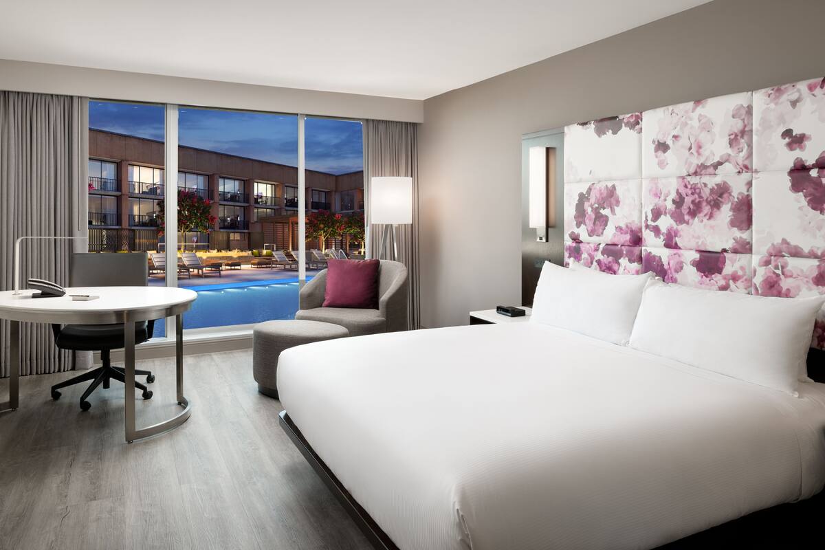 A hotel room with a large bed, a desk, and a view of a swimming pool and building.