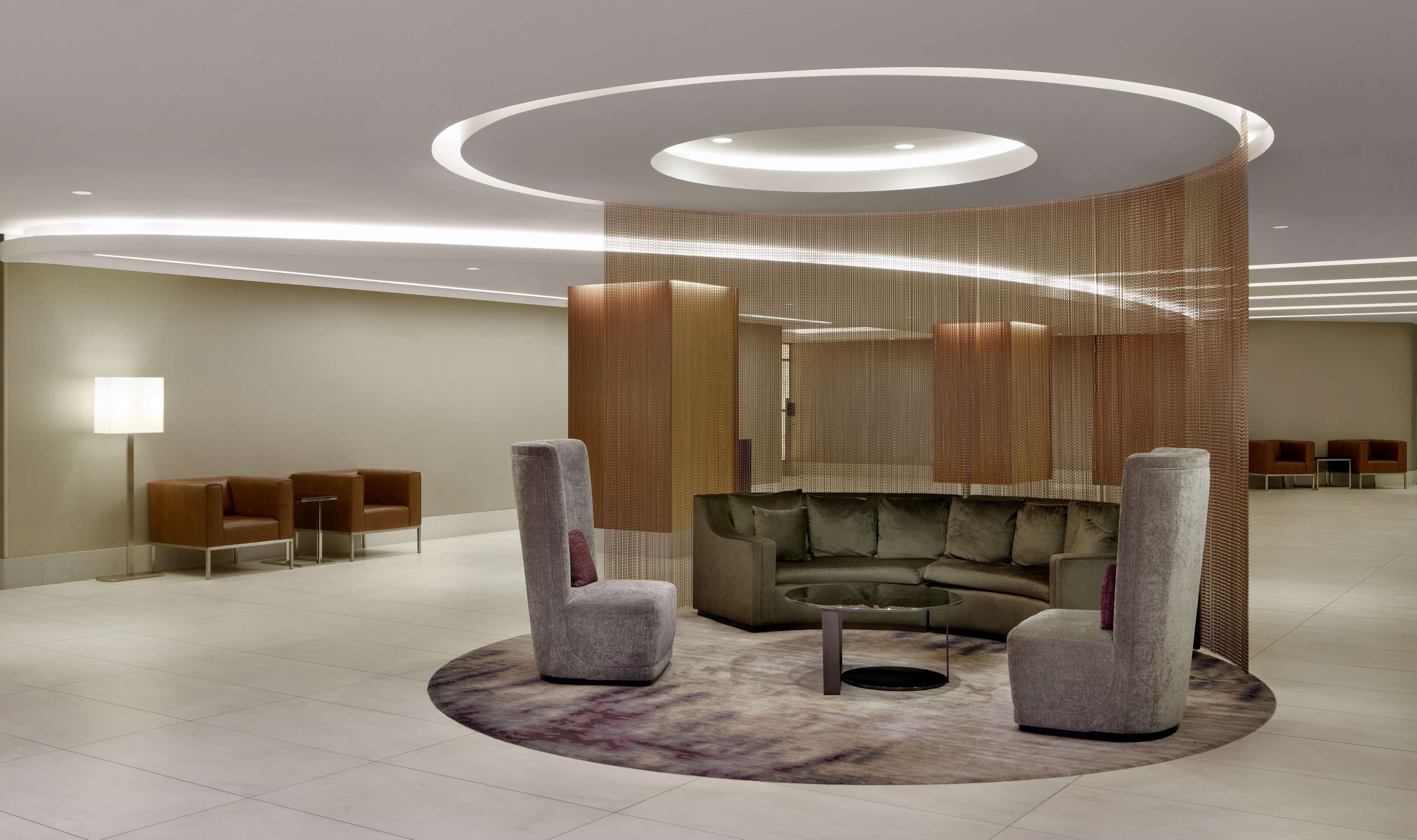 A modern lounge area with a circular seating arrangement, a patterned rug, and a unique ceiling design with recessed lighting.