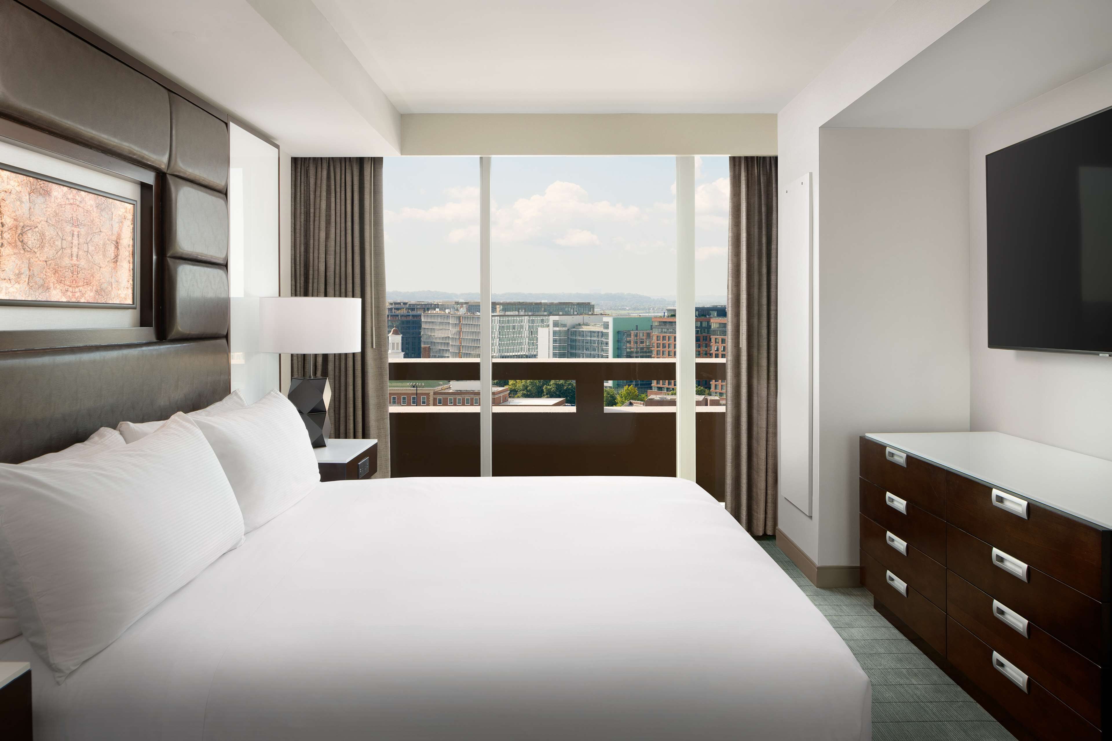 A hotel room with a large bed, a dresser, a flat-screen TV, and a city view.