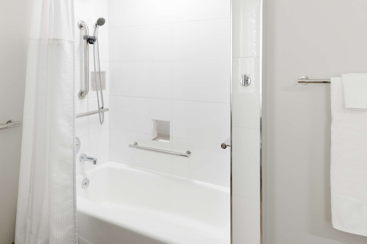 Uma casa de banho moderna com uma banheira branca, um chuveiro com porta de vidro e um porta-toalhas.