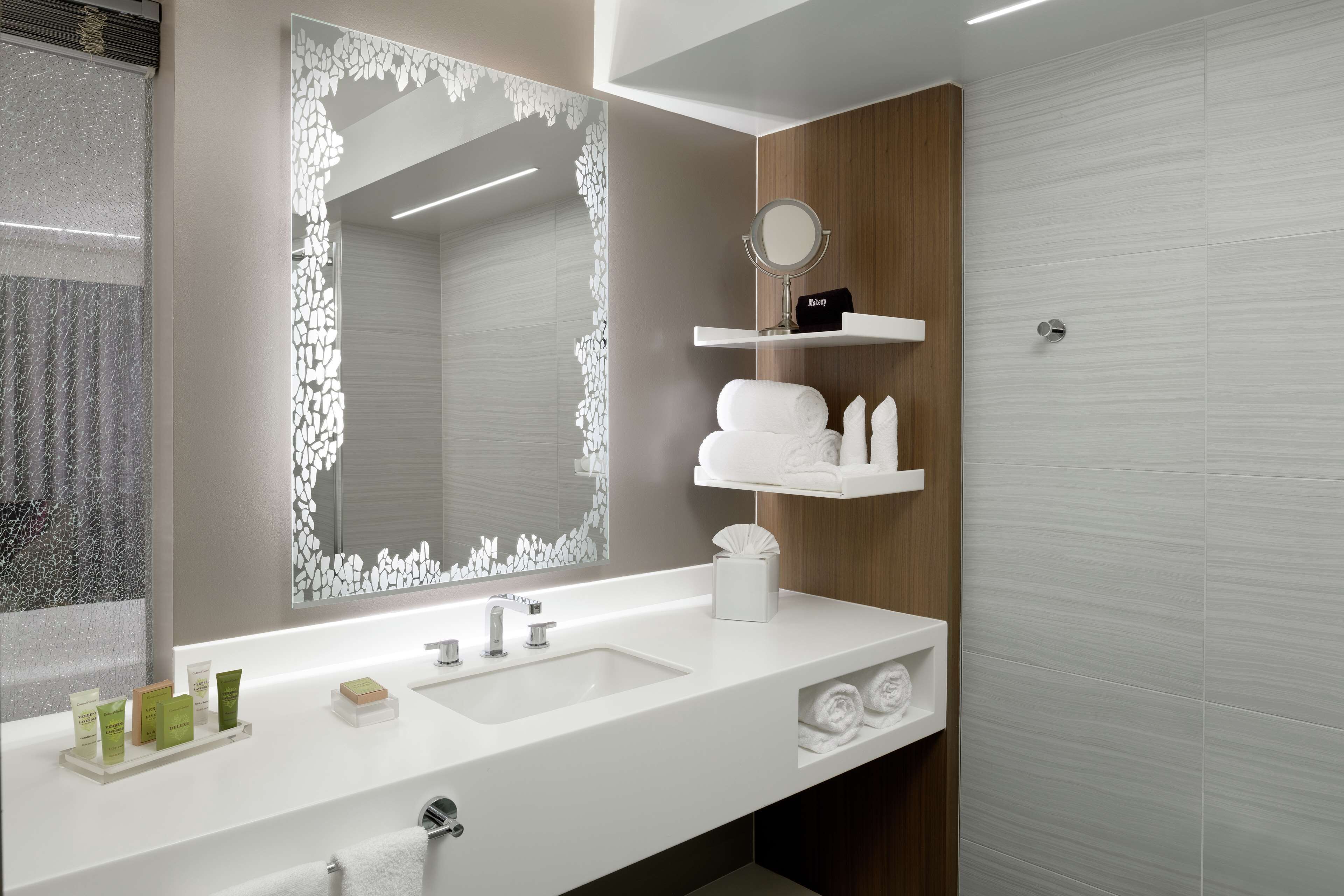 A modern bathroom with a white sink, a large mirror with a decorative frame, and a wooden panel on the wall.