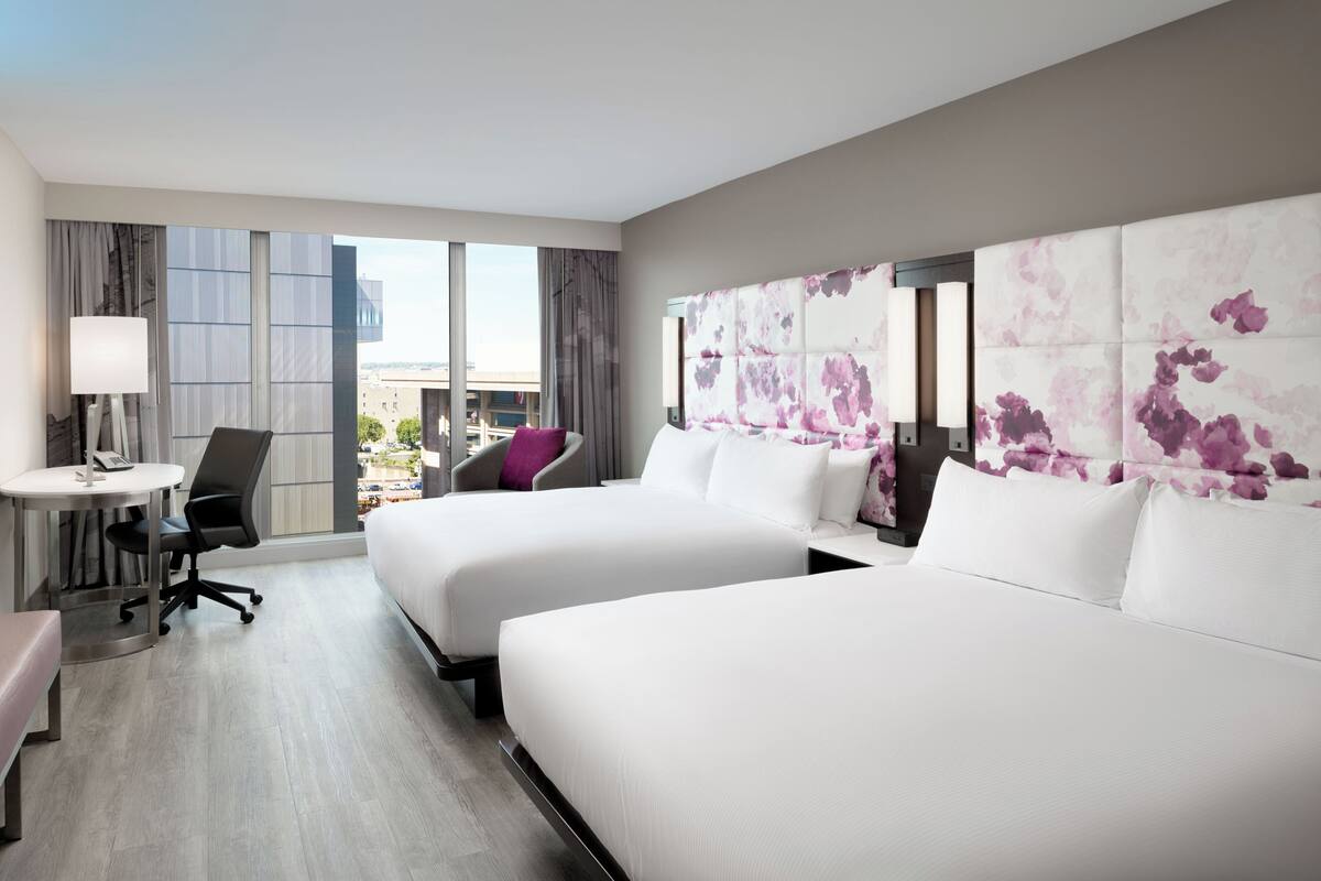 A hotel room with two beds, a desk, a chair, and a large window.