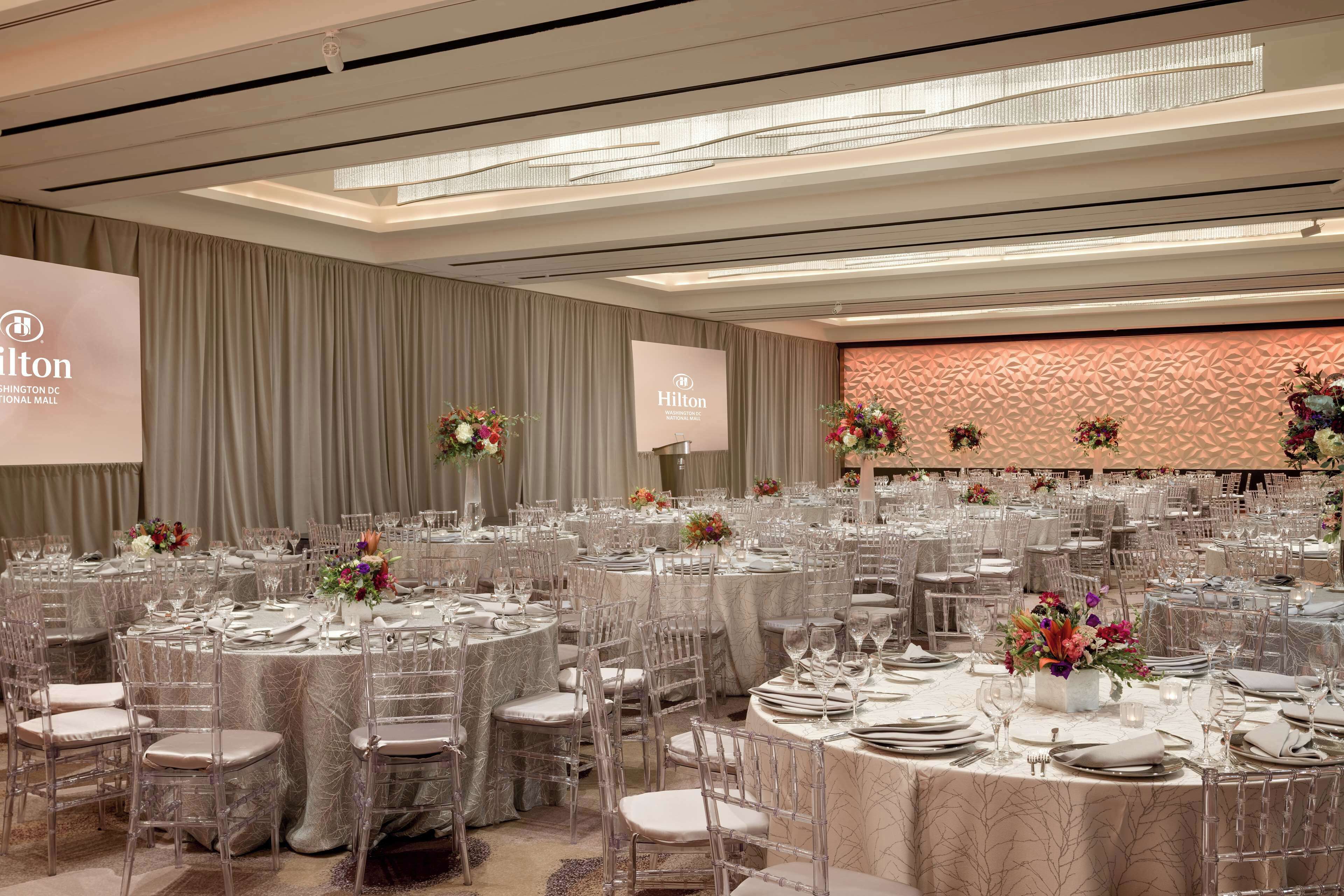A spacious event space with round tables, clear chairs, and floral centerpieces.