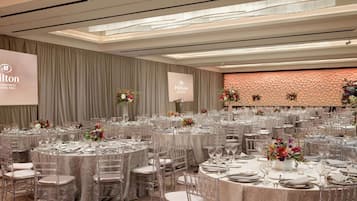 A spacious event space with round tables, clear chairs, and floral centerpieces.