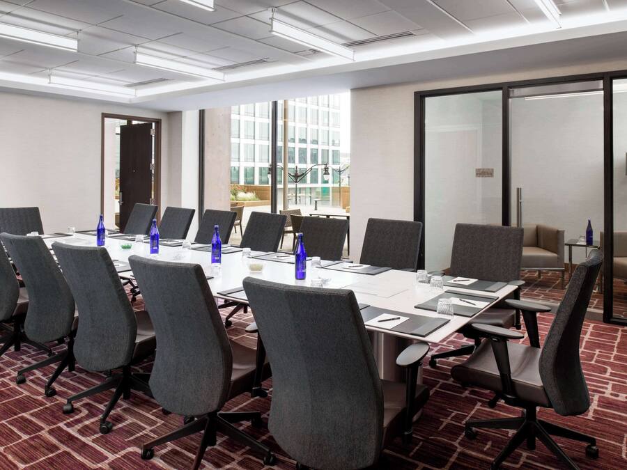 Uma sala de conferências com uma mesa grande, várias cadeiras e piso coberto de carpete.