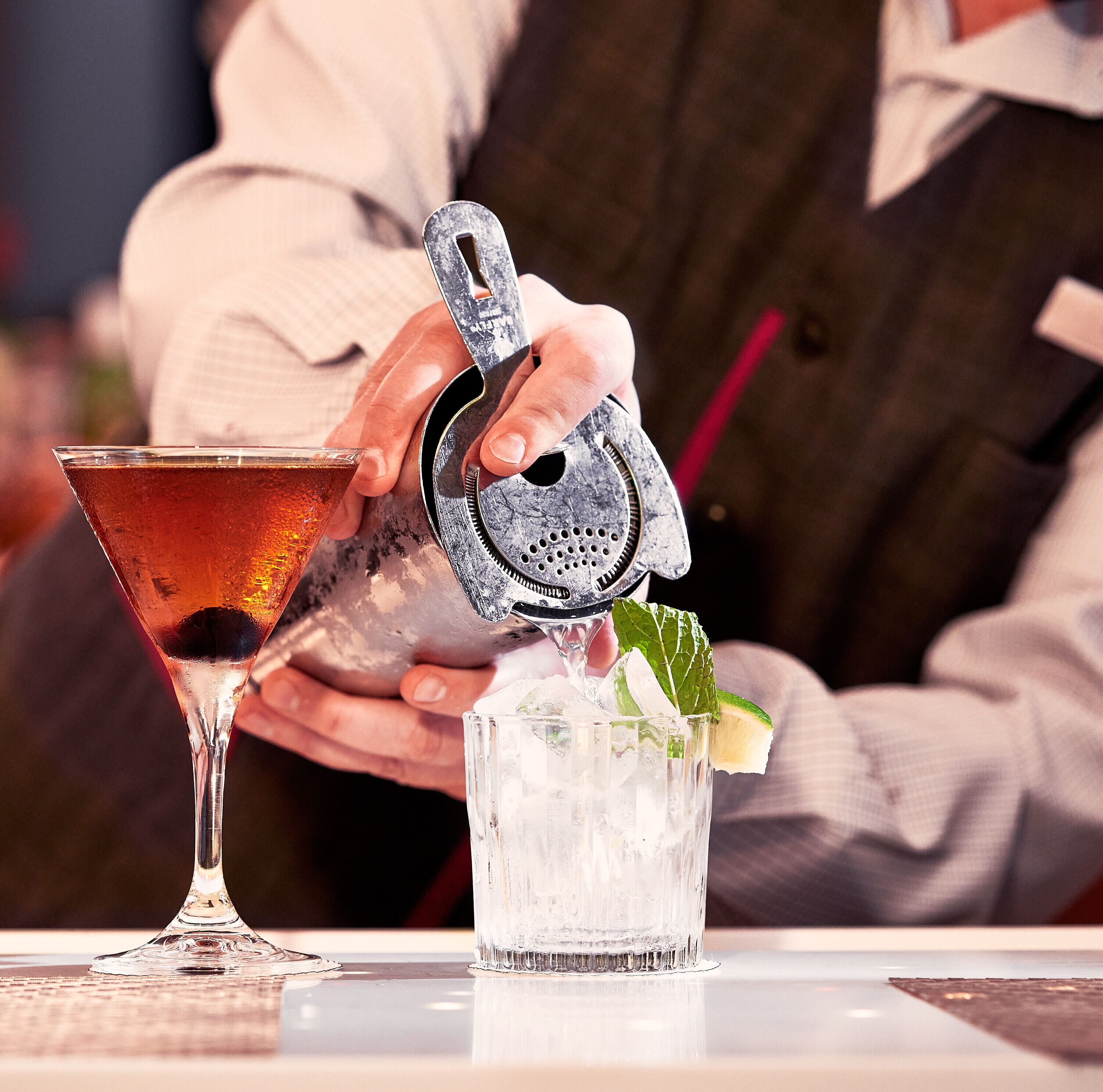 Um bartender servindo uma bebida em um copo com gelo e uma fatia de limão.