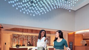 A lobby with a modern ceiling design, a reception desk, and two individuals with luggage. - Hilton Washington DC National Mall The Wharf (Washington)