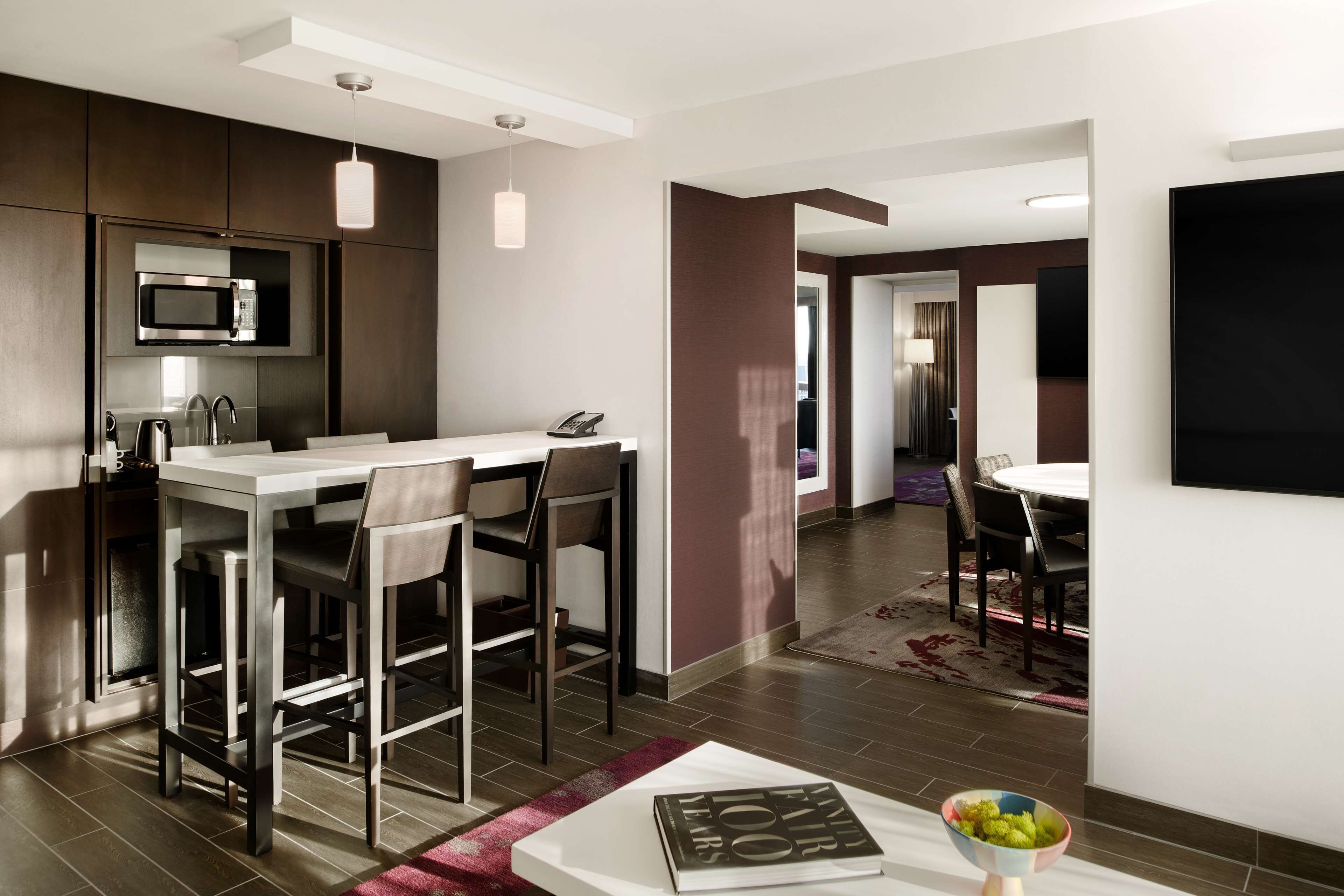 A modern kitchen with a built-in microwave, a dining area with a white table and chairs, and a living area with a flat-screen TV.
