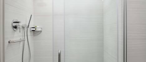 A modern shower with a handheld showerhead, a wall-mounted control panel, and a glass door.