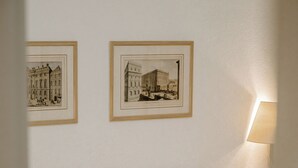 Una cama bien hecha con sábanas blancas y un cojín beige, fotografías en blanco y negro en la pared, y una lámpara de noche.