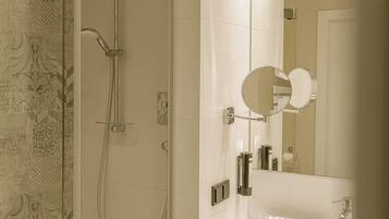 Un bagno moderno con doccia vetrata, lavandino bianco con asciugamano con la scritta “MAKE UP” e specchio a cornice rotonda.