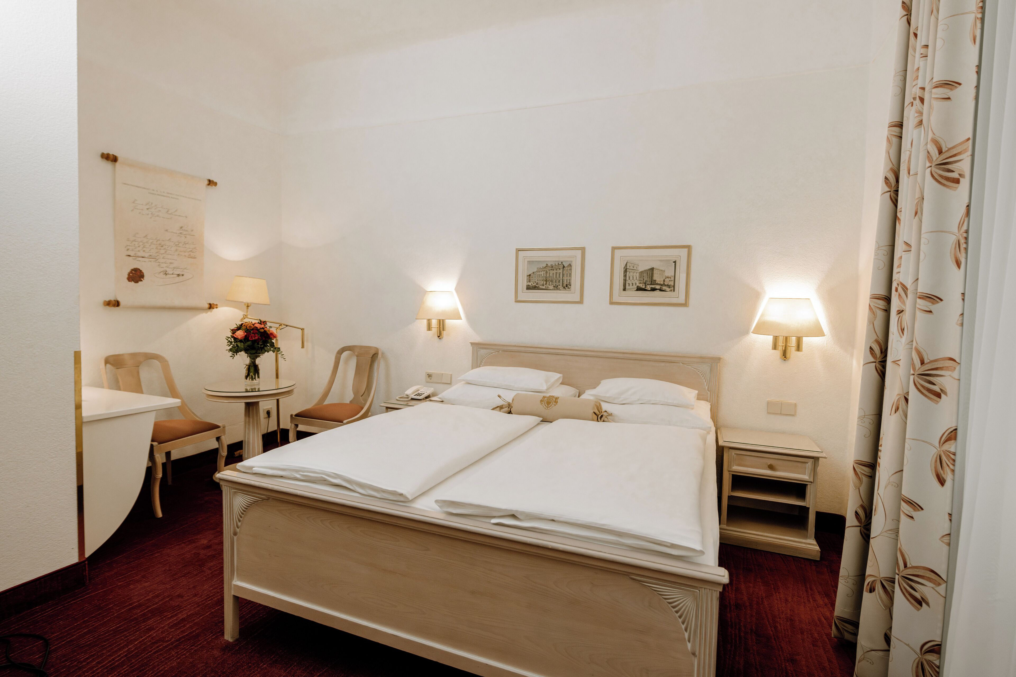 Ein Hotelzimmer mit einem großen Bett, zwei Nachttischen, einem Sessel, einem kleinen Tisch mit einer Lampe und zwei gerahmten Bildern an der Wand.