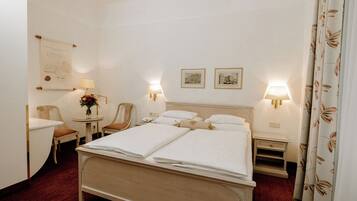 A hotel room with a large bed, two bedside tables, a chair, a small table with a lamp, and two framed pictures on the wall.