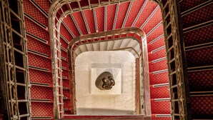 Una escalera de caracol con un muro de pared con diseño rojo y una plaza central con una escultura.