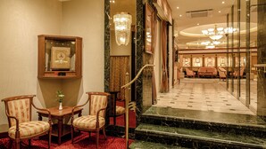 Un hall de hotel con una escalera de mármol, un candelabro y un área de descanso con sillas y una mesa.