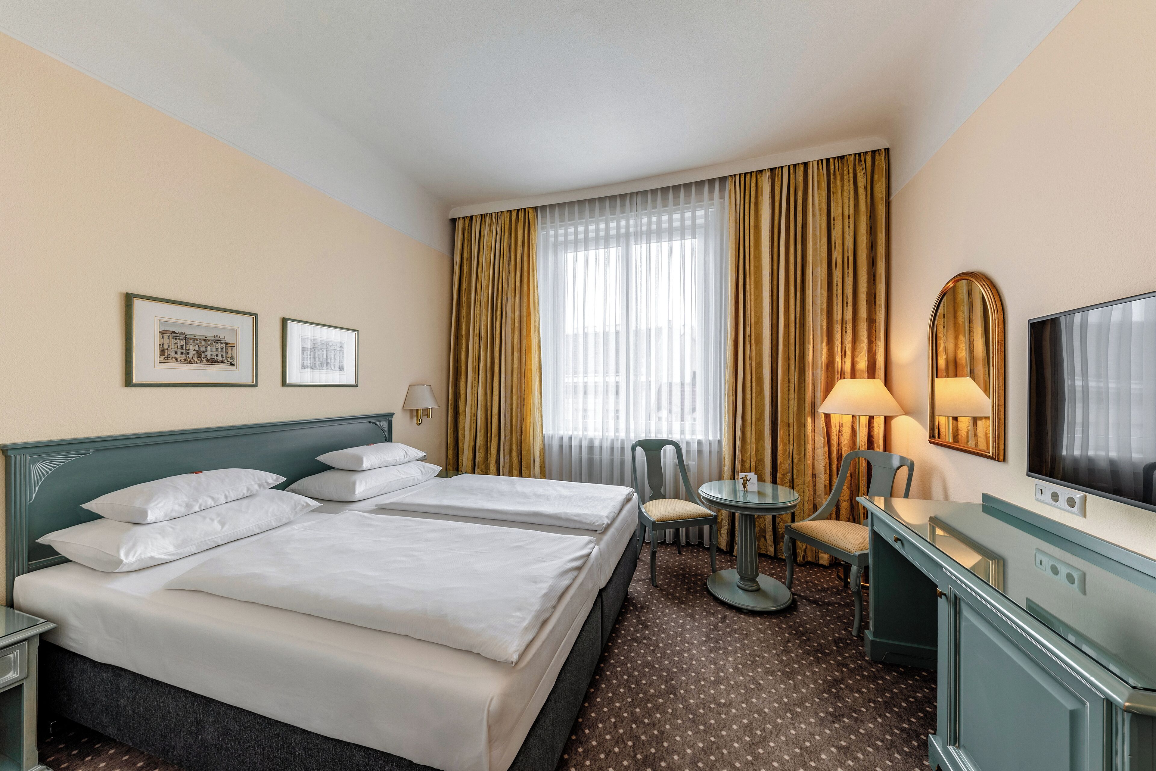 Quarto de hotel com duas camas, uma escrivaninha, uma cadeira, uma televisão e uma janela com cortinas.