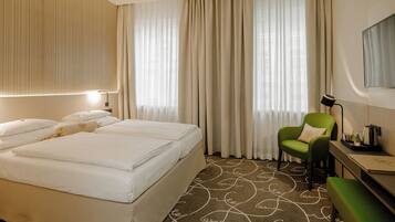 Una habitación de hotel con una cama grande, un sillón verde, un escritorio y una televisión.