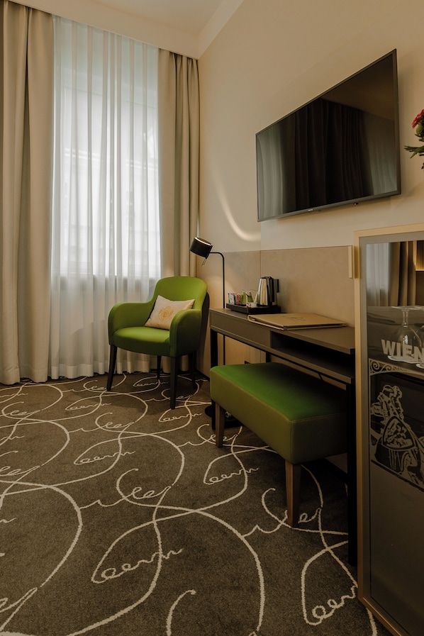 A hotel room with a green armchair, a desk with a laptop, a flat-screen TV mounted on the wall, and a minibar. - Hotel Erzherzog Rainer (Vienna)