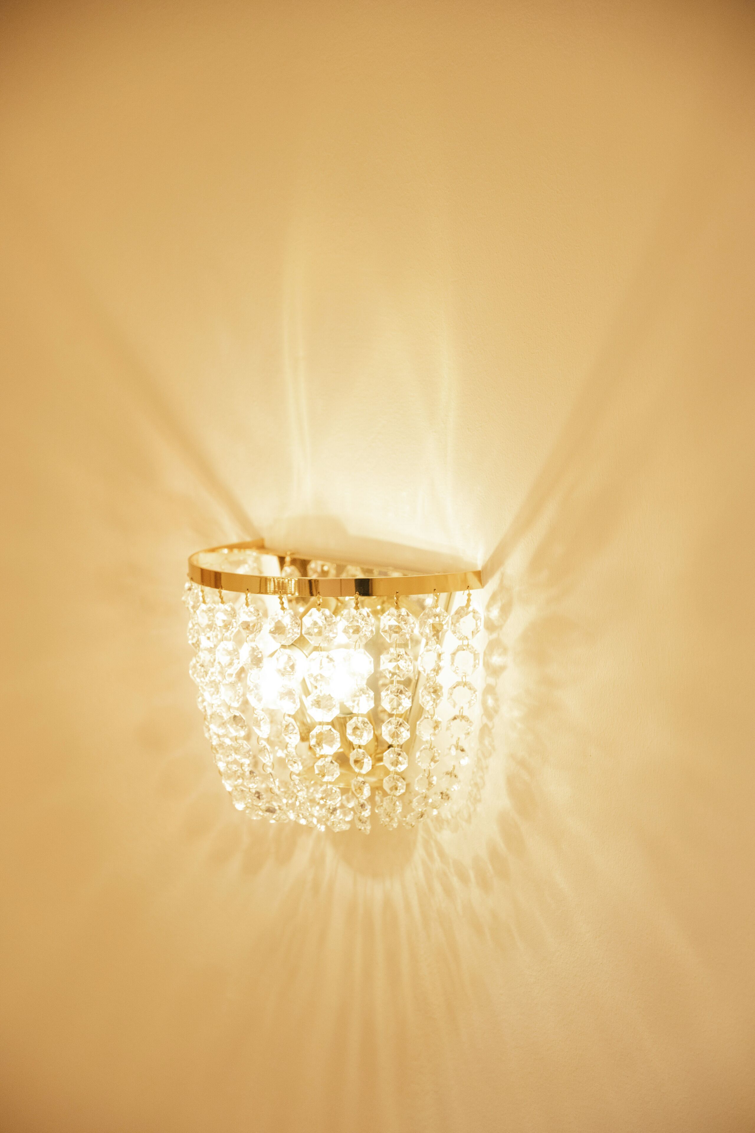 A wall-mounted light fixture with a cylindrical shape and a gold-colored base, surrounded by numerous clear crystal-like elements.