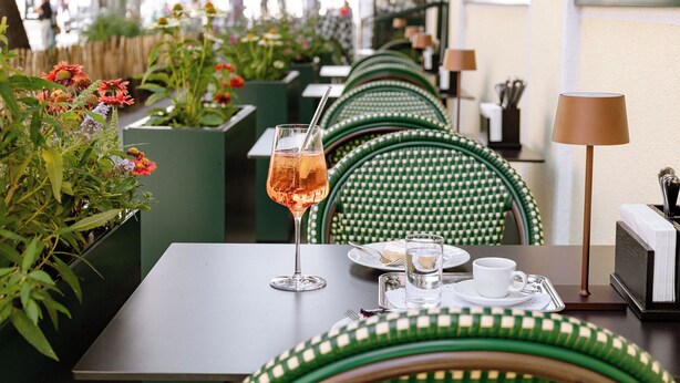 Una fila de sillas blancas y verdes a cuadros con una mesa dispuesta para dos, incluyendo un vaso de bebida y una taza de agua.