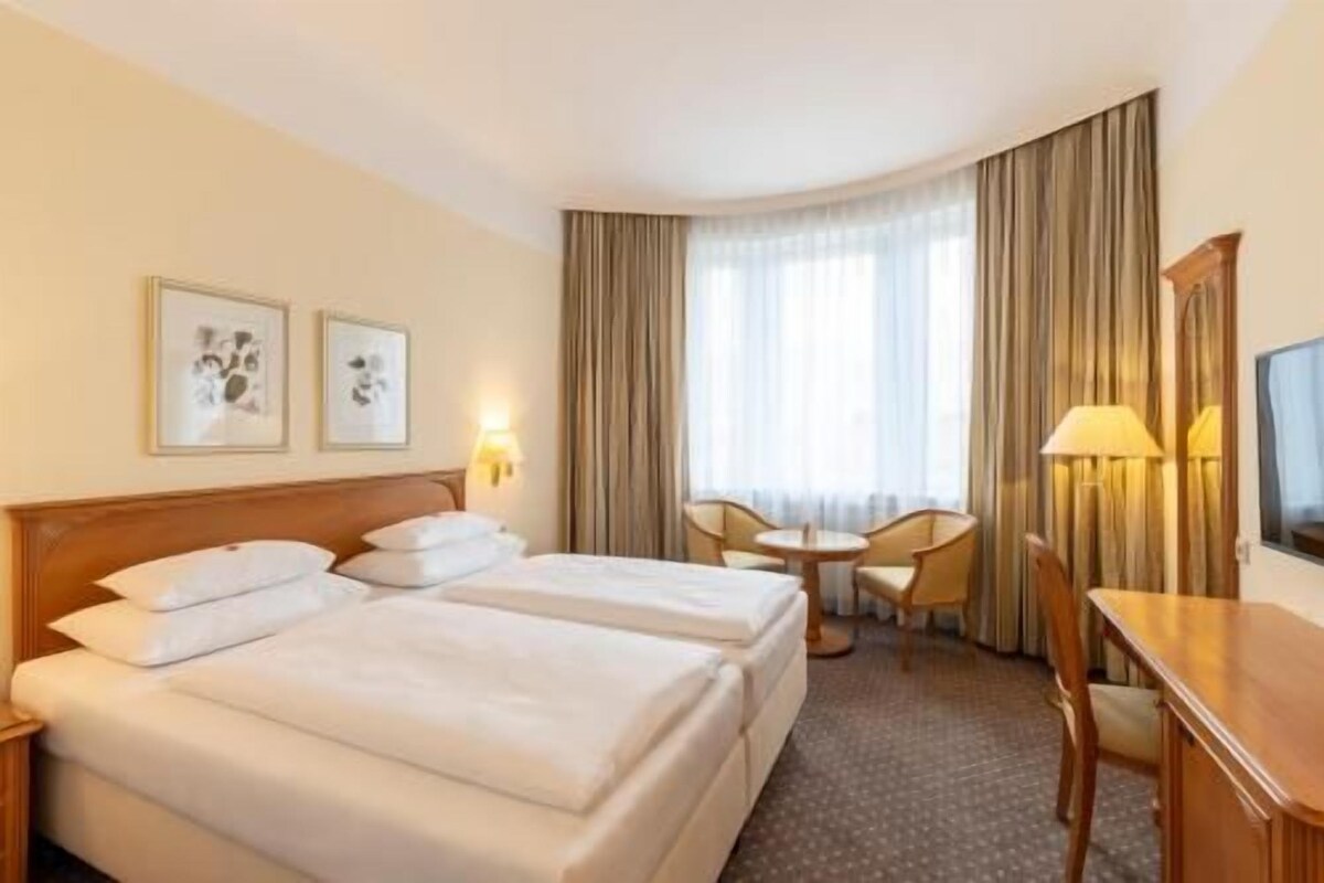 A hotel room with two beds, a desk, a chair, and a television.