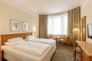 Een hotelkamer met twee bedden, een bureau, een stoel, een klein tafeltje en een televisie.