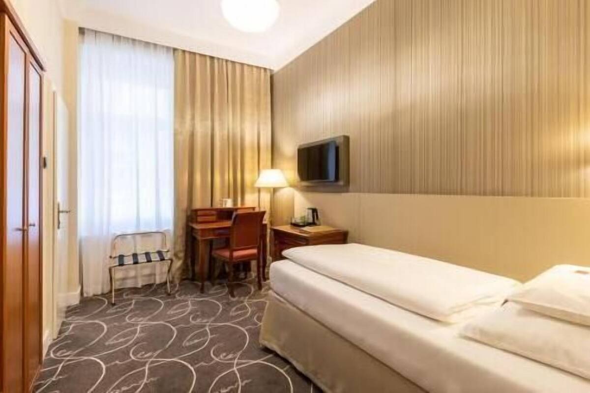 A hotel room with a bed, a desk with a chair, a television, and a window with curtains.