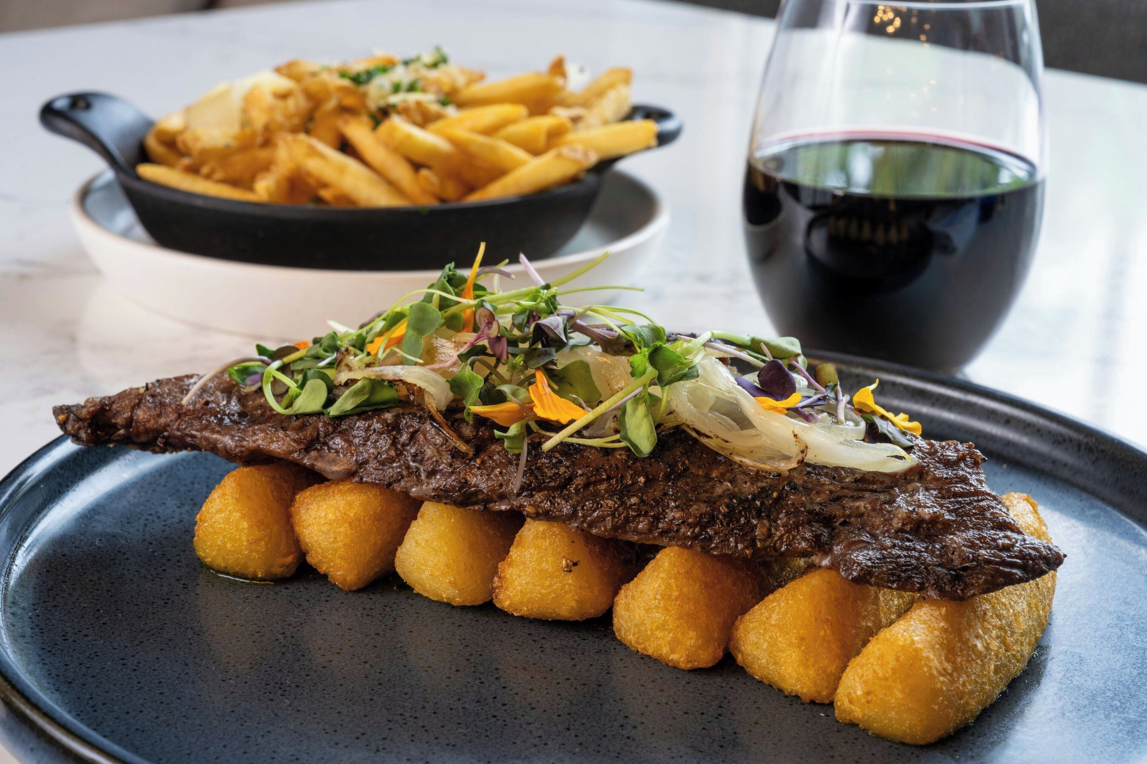 Une assiette de steak accompagné de légumes et de pommes de terre, un bol de frites et un verre de vin rouge.
