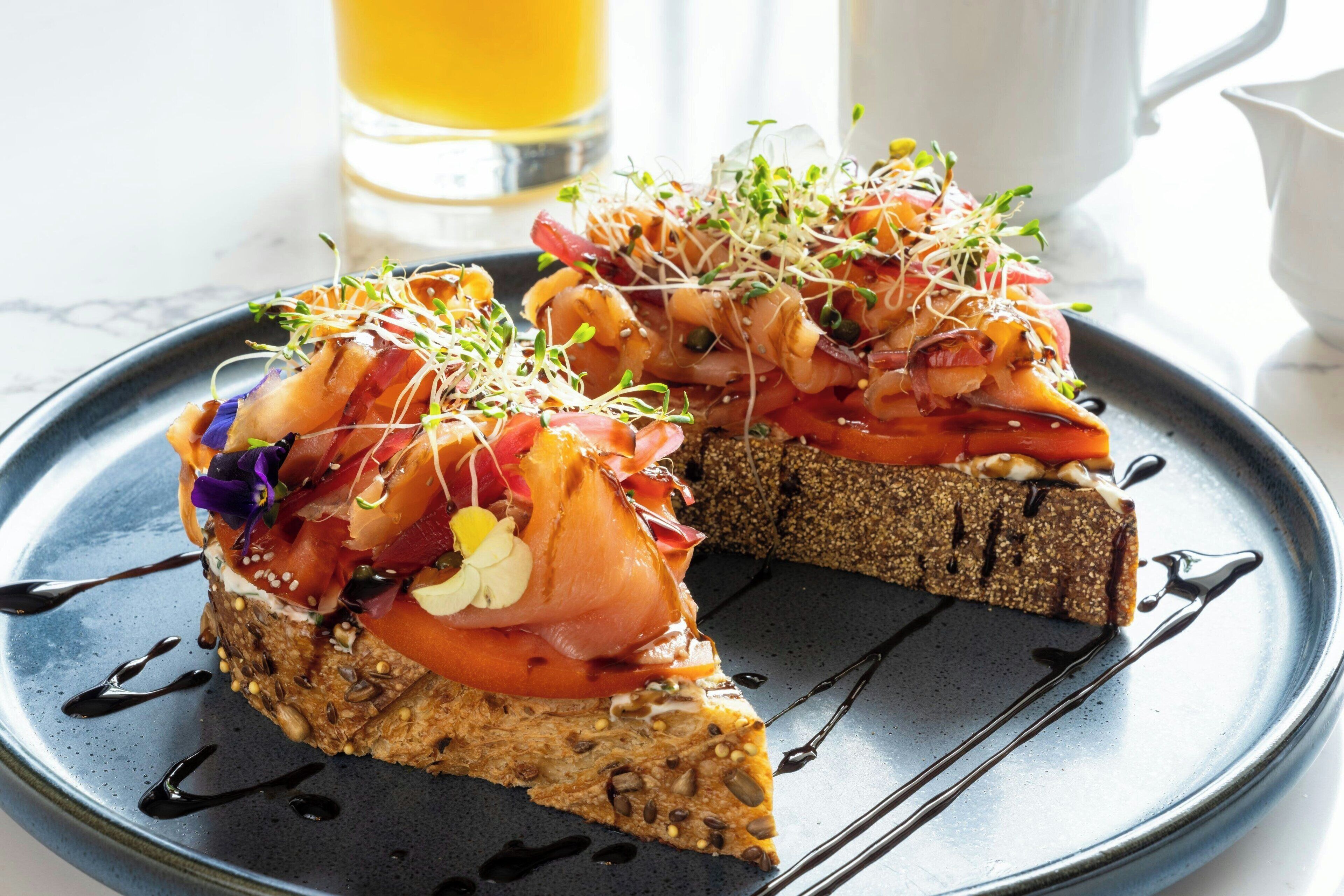 A slice of toast topped with salmon, vegetables, and sprouts on a plate.