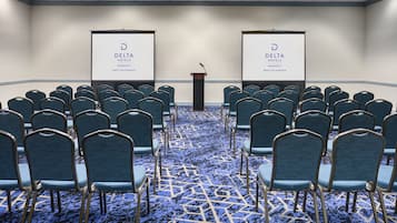 A conference room with rows of chairs, a podium, and two screens displaying 'Delta Hotels Marriott West Palm Beach'.