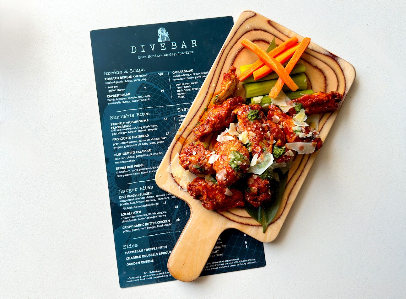 A menu with various food items and a wooden board with a dish of chicken wings garnished with vegetables.