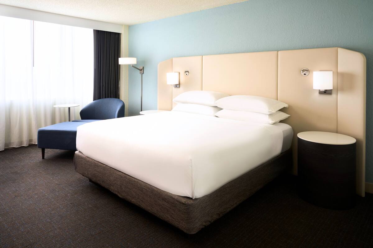 A hotel room with a large bed, a chair, a bedside table, and a lamp.