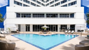 A modern hotel with a large outdoor swimming pool, lounge chairs, and umbrellas.