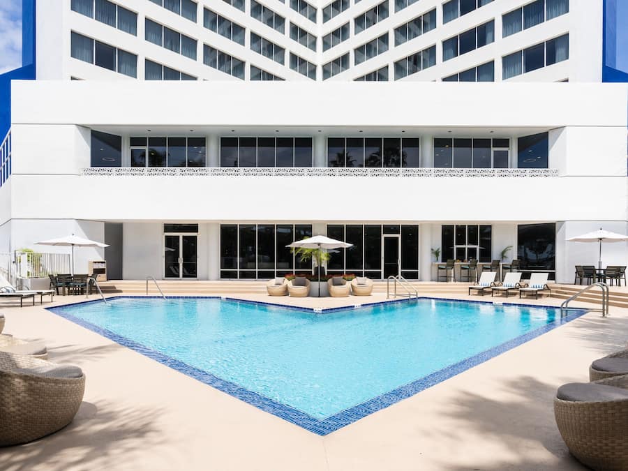 Un hotel moderno con una gran piscina exterior, sillas de descanso y sombrillas.