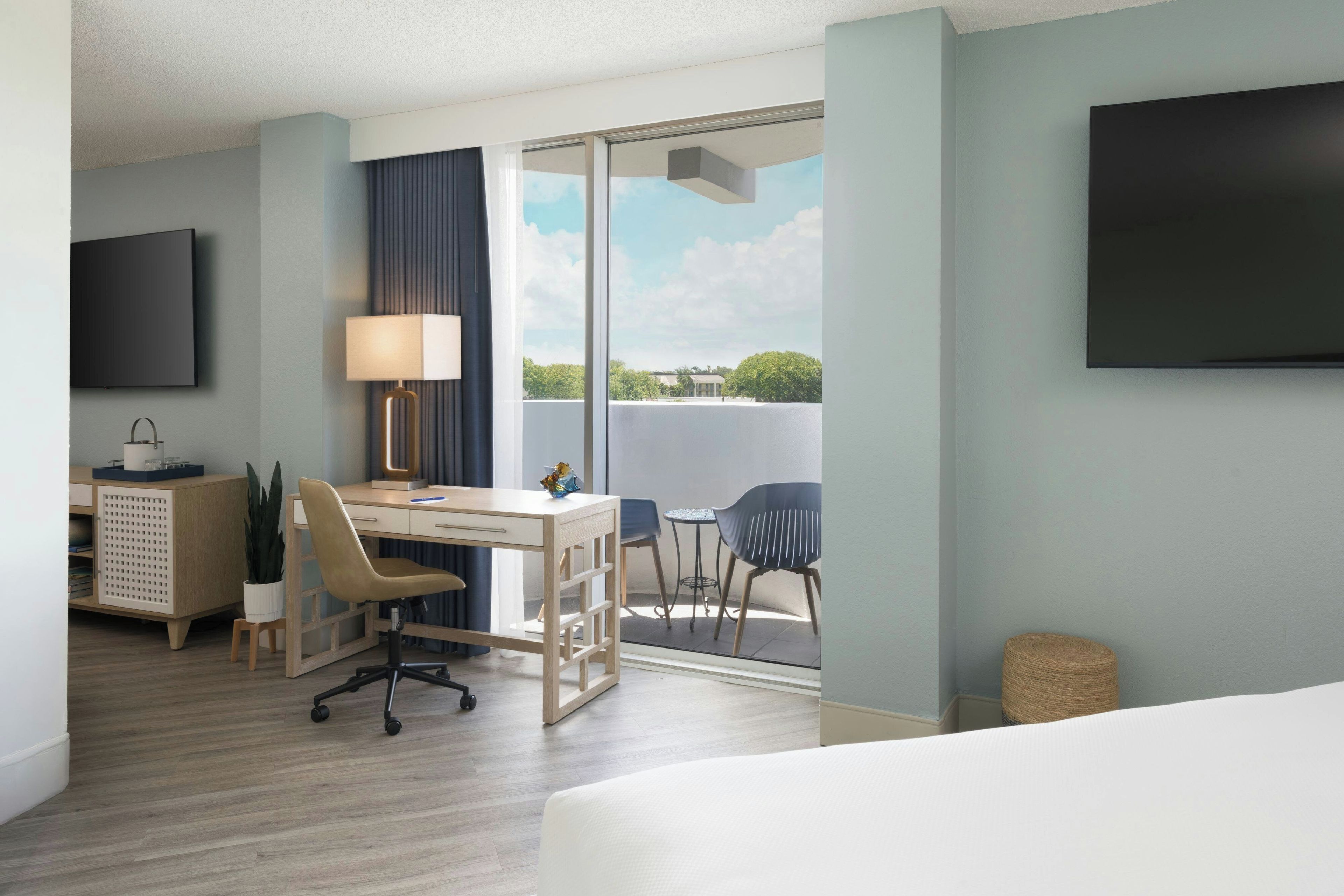 Ein Hotelzimmer mit Bett, Schreibtisch mit Stuhl, Fernseher und Balkon mit Sitzgelegenheiten.