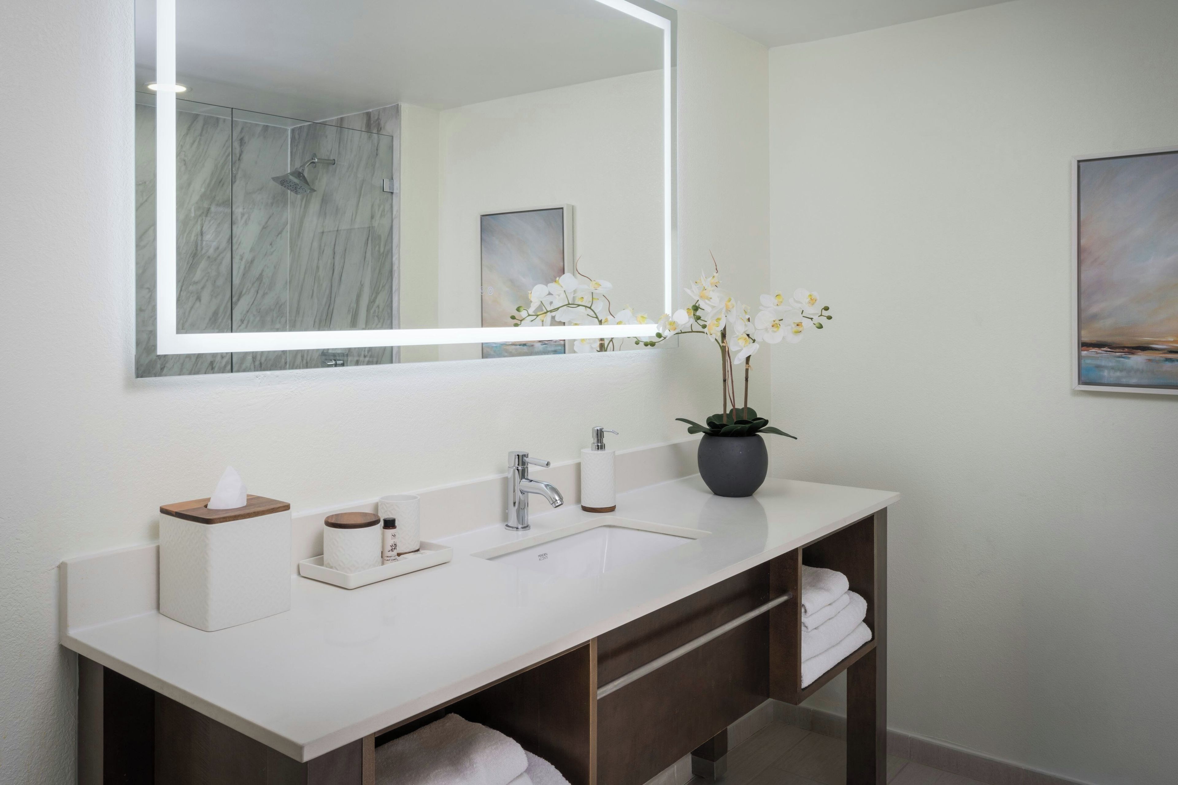 Une salle de bain moderne avec un grand miroir, un lavabo blanc, une douche et un porte-serviettes.