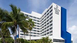 A modern Delta Hotels Marriott building with a white facade and blue accents, surrounded by palm trees.