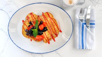 A plate of food with a blue rim, a glass of a beverage, and a striped napkin with cutlery on a marble surface.