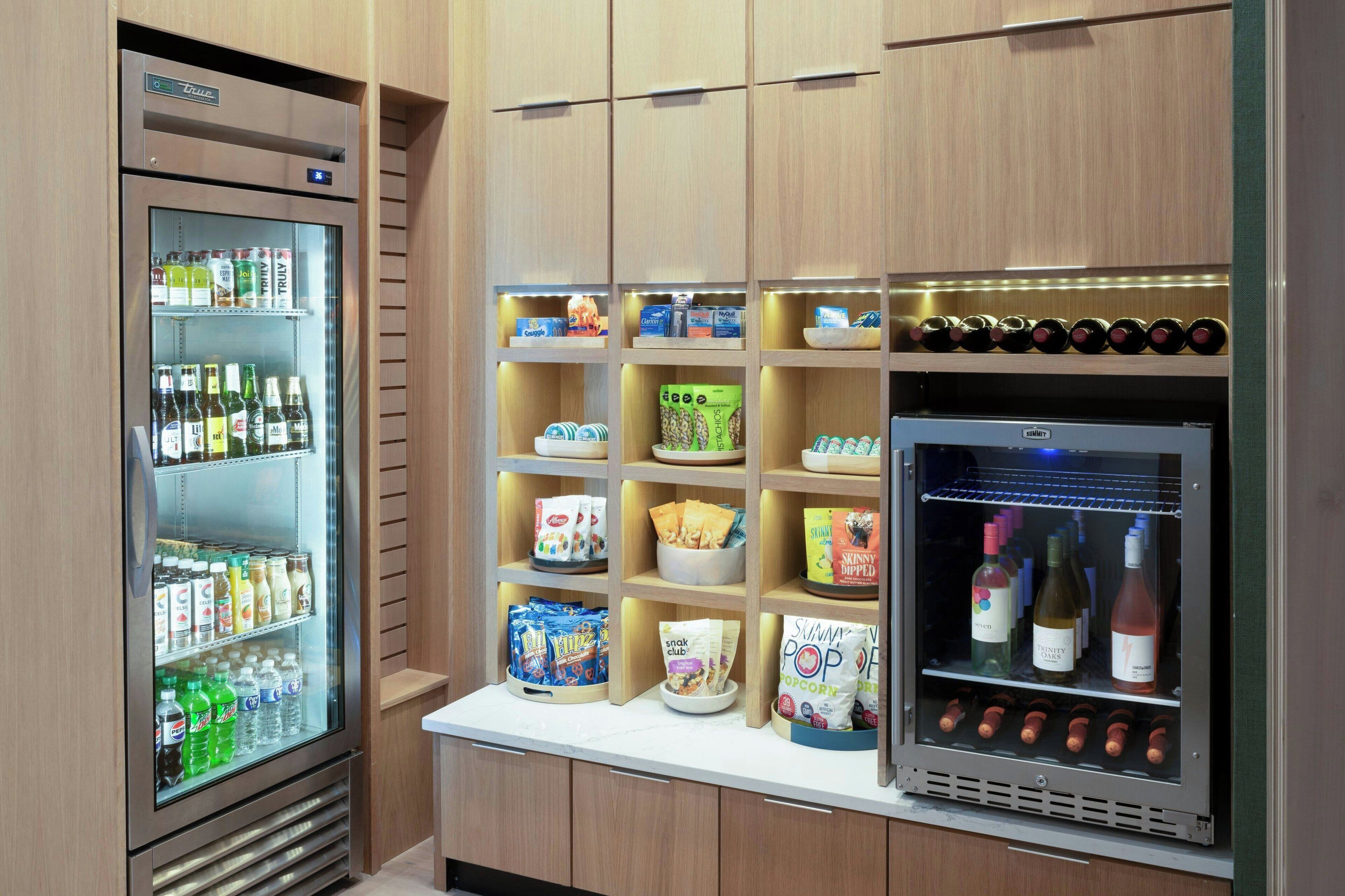 Uma cozinha compacta com geladeira repleta de bebidas e lanches, micro-ondas e adega para vinhos.