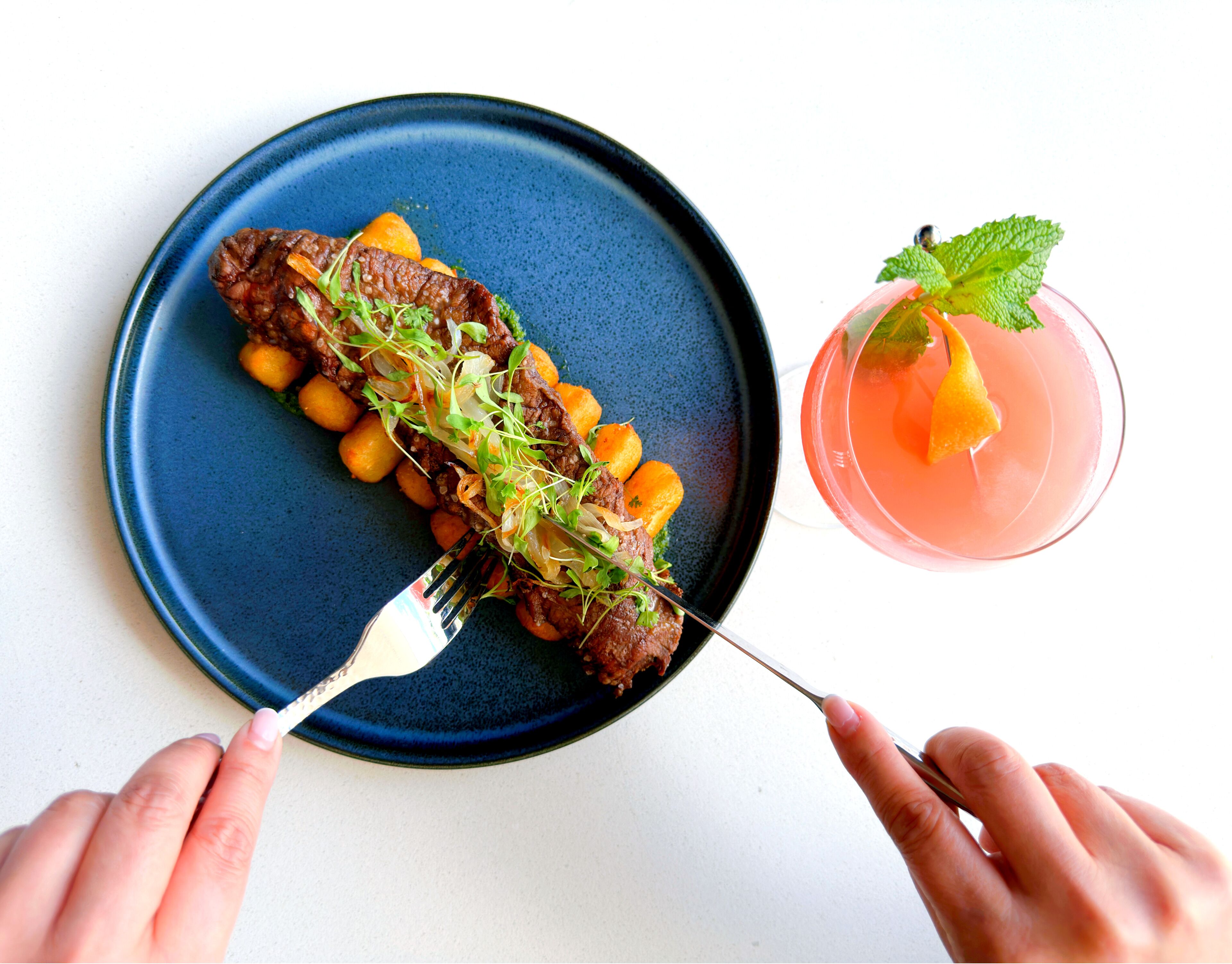 A plate with a steak and vegetables, and a cocktail with a mint garnish.