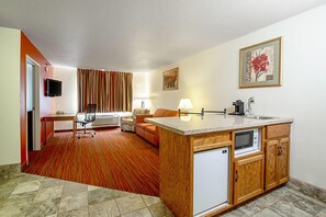 A compact hotel room with a kitchenette, a seating area with a sofa and armchair, a television, and a painting on the wall. - Quality Inn Aberdeen (Aberdeen)