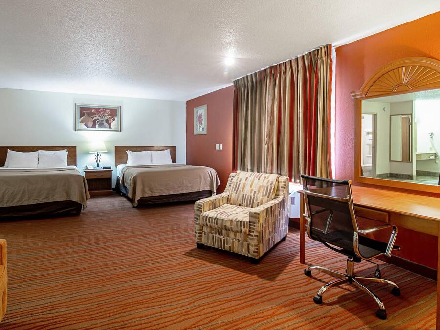 A hotel room with two beds, a desk, a chair, a mirror, and a carpeted floor.