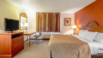 A hotel room with a bed, desk, chair, television, and a window with curtains.