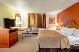 A hotel room with a bed, desk, chair, television, and a window with curtains.