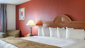 A hotel room with a large bed, a wooden headboard, a bedside lamp, a chair, and a painting on the wall.