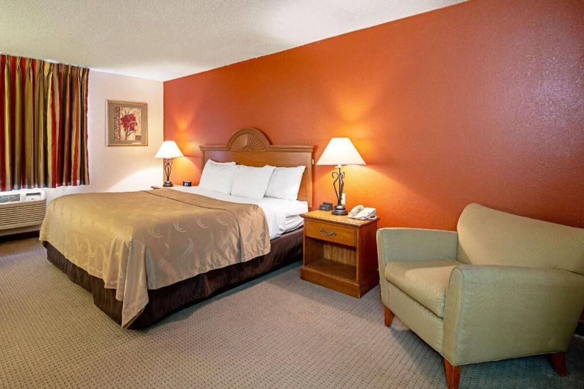A hotel room with a bed, bedside lamps, a nightstand, a chair, and a wall-mounted artwork.