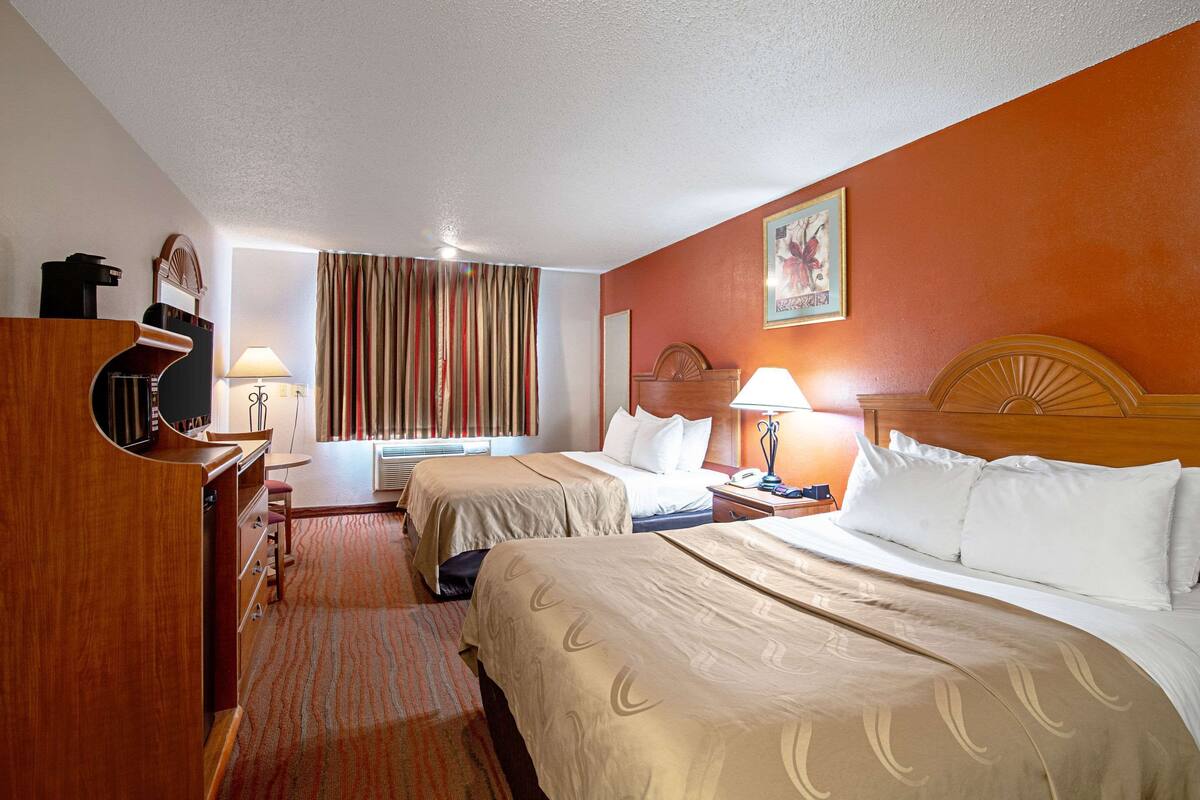 A hotel room with two beds, a desk, a chair, a lamp, and a window with curtains.