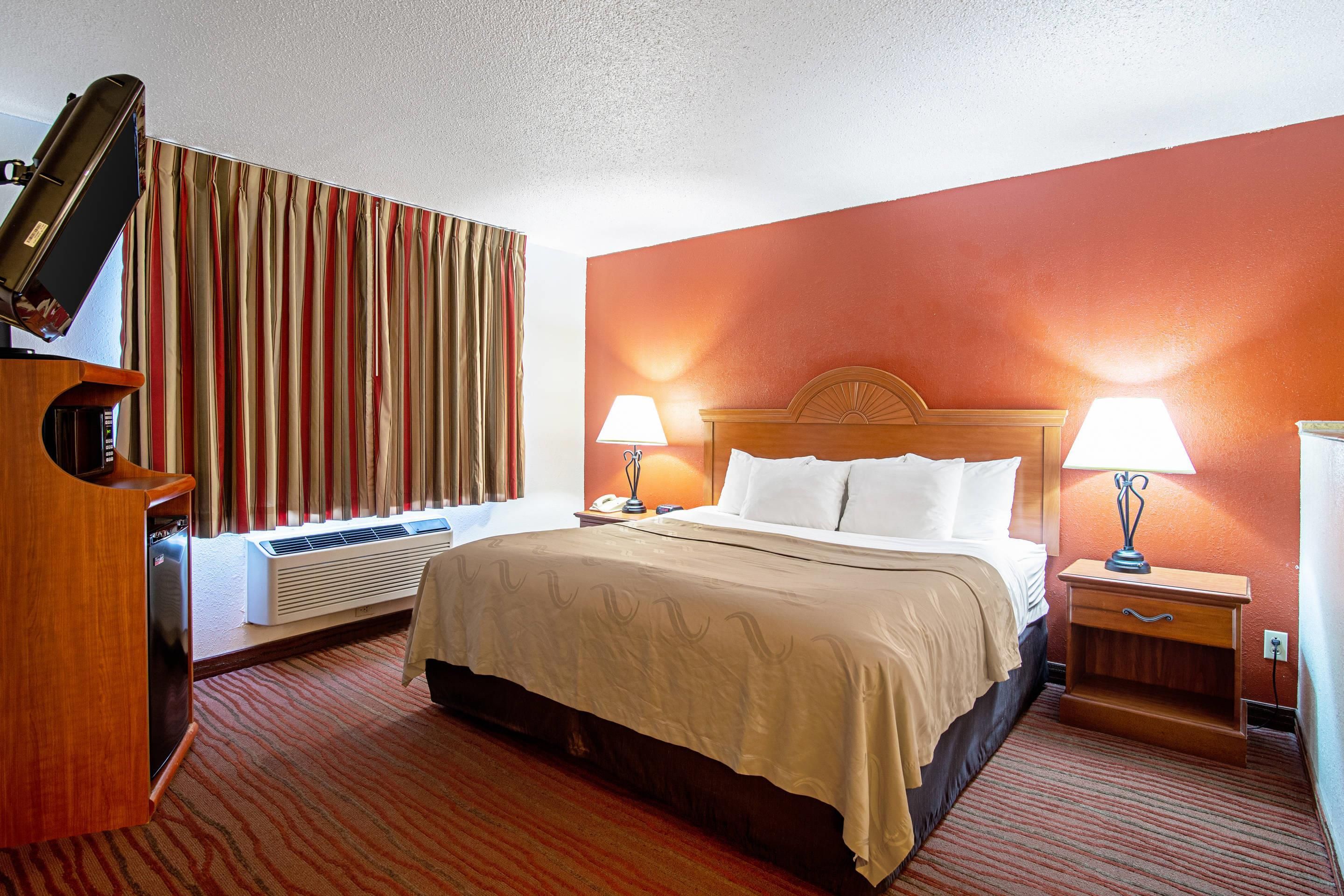A hotel room with a bed, bedside lamps, a desk with a lamp, a television, and a window with curtains.